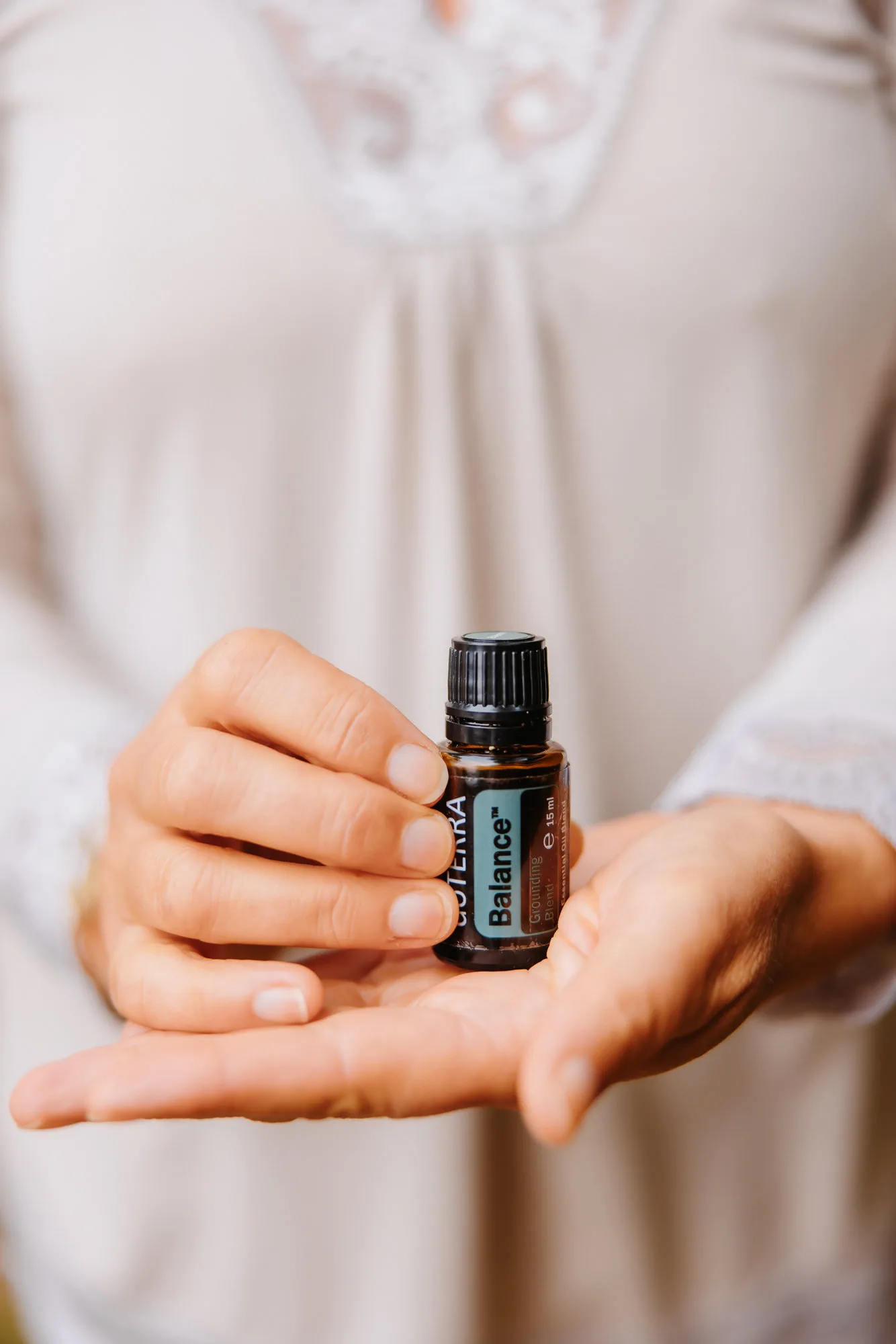 Close-up of a woman’s hands holding dōTERRA Balance essential oil.