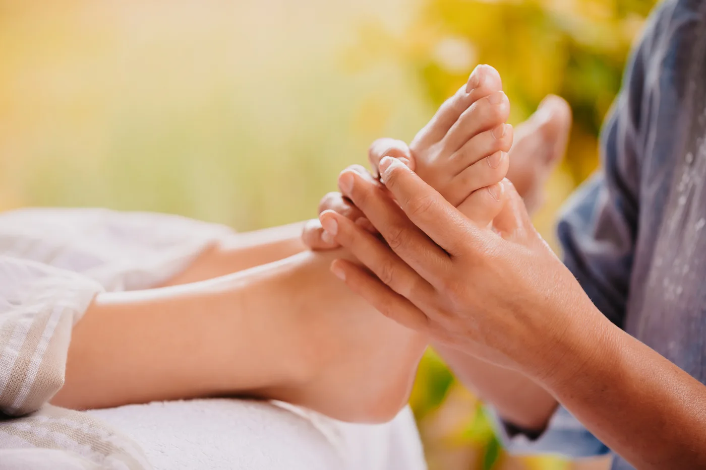 A woman’s hands performing a foot reflexology massage on feet resting comfortably on the treatment table