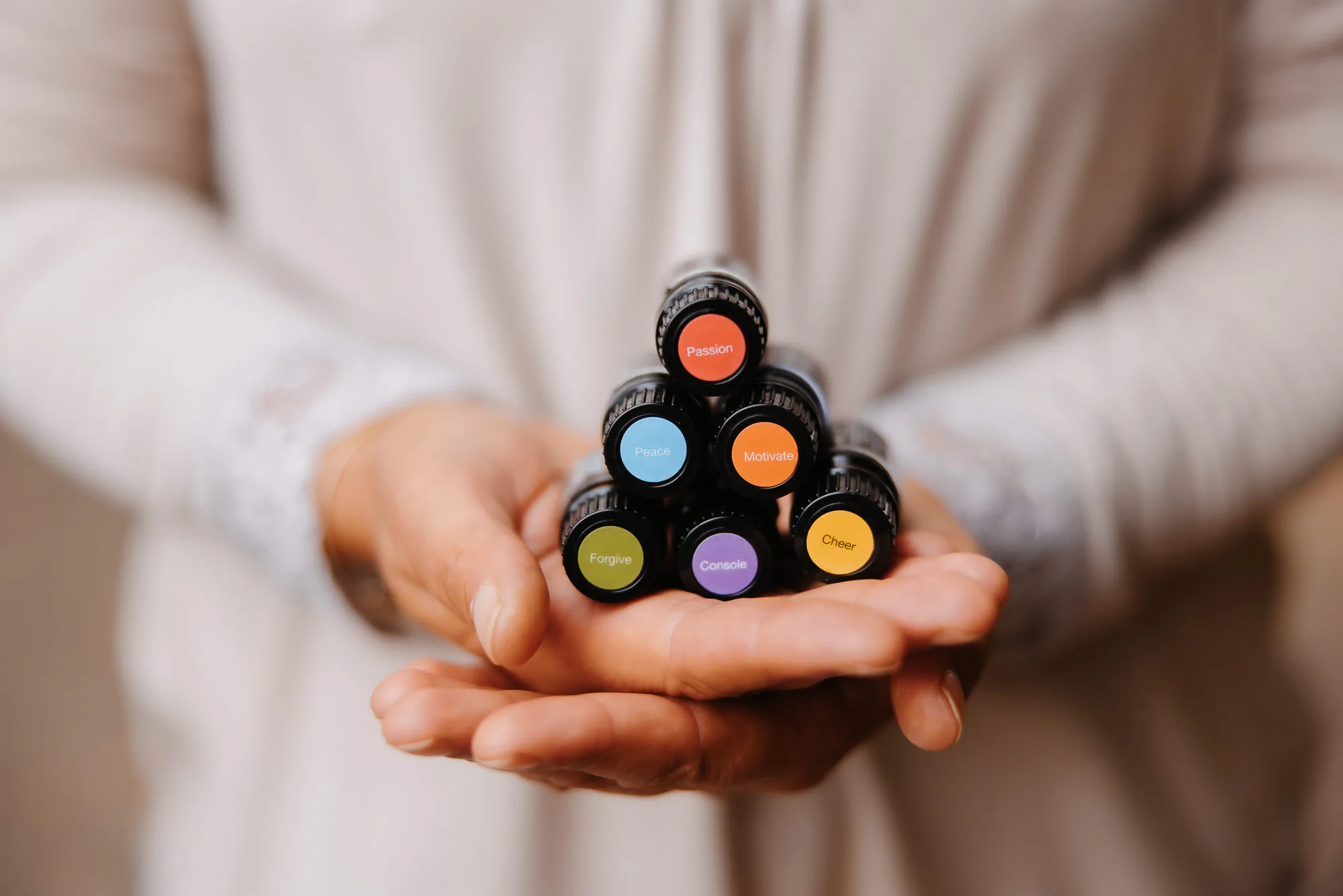 Close-up of a woman’s hands holding the essential oils from the dōTERRA Emotional Aromatherapy Collection, arranged in a pyramid 